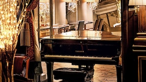 A grand piano in a warmly lit room with elegant chandeliers and draped curtains. - Le Meurice - Dorchester Collection (Paris)