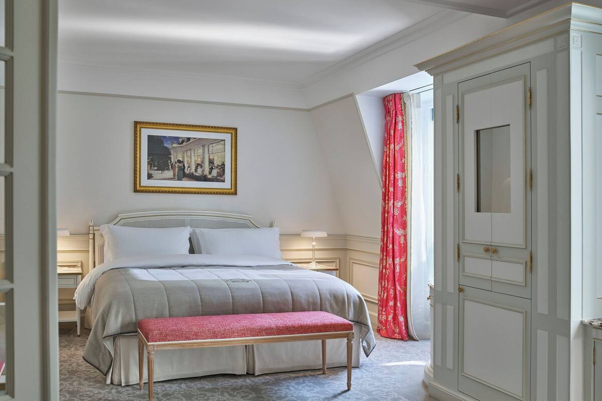 A bedroom with a bed, bedside tables, a bench, a wardrobe, and a framed picture on the wall.