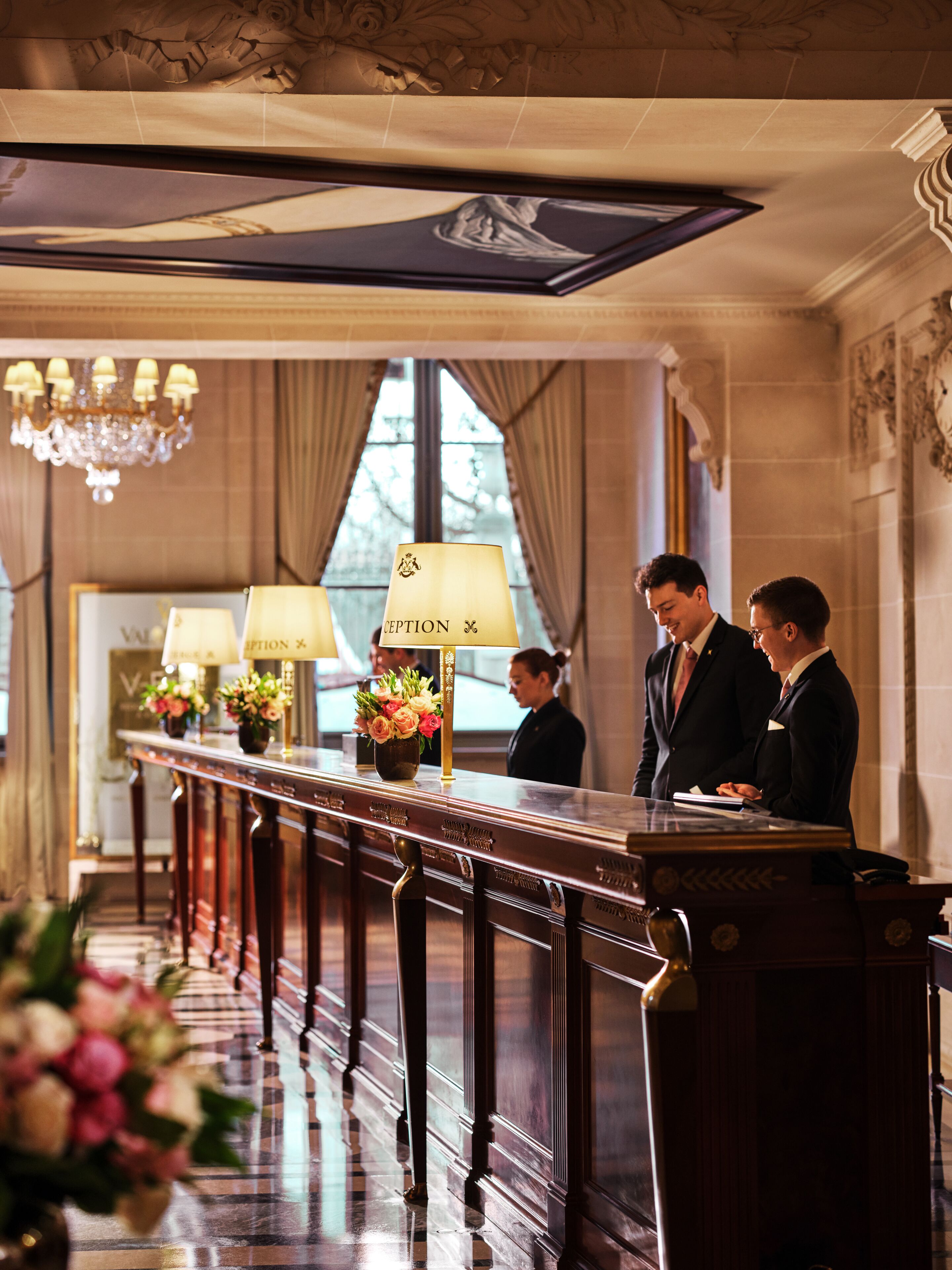 A reception desk with a chandelier, a reception area, and a view of the outside through large windows.