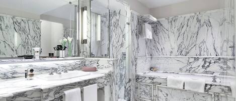 A modern bathroom with marble walls and floors, a large mirror, and a shower area.