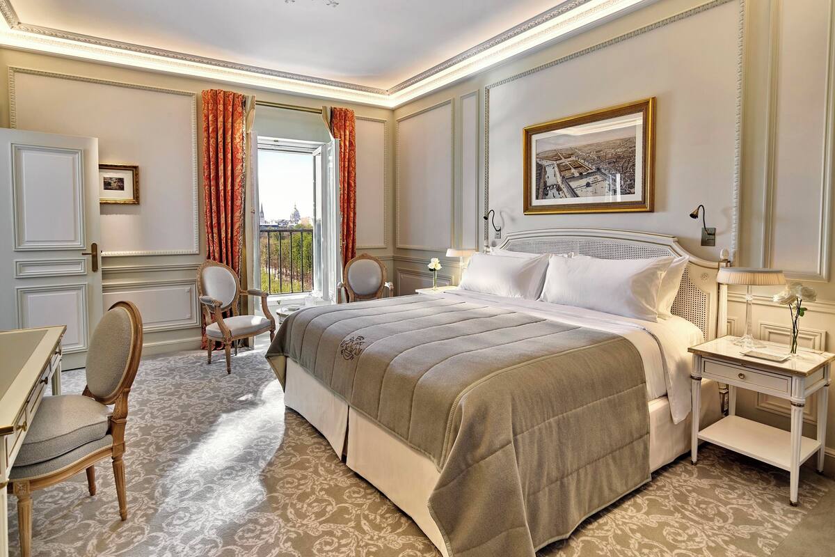 A well-appointed bedroom with a large bed, a desk, and chairs, featuring a balcony view.