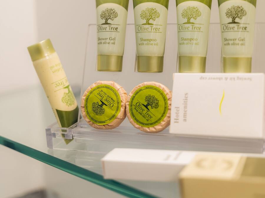 Une sélection de gel douche et de shampoing de la marque Olive Tree est exposée sur une étagère en verre.