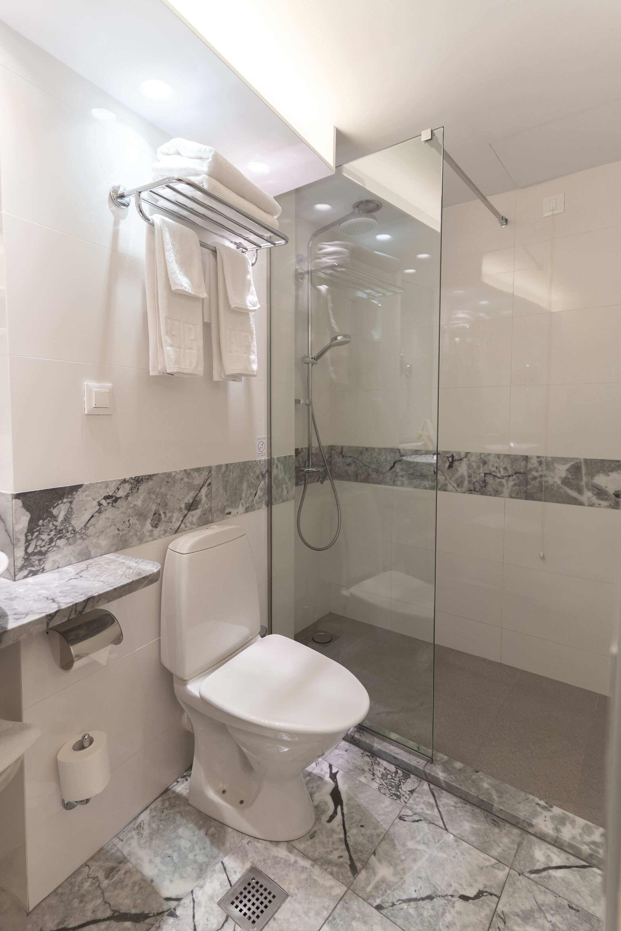 A modern bathroom with a glass-enclosed shower, a white toilet, and a marble-tiled floor.