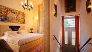 A hotel room with a bed, a chandelier, a painting, and a staircase.