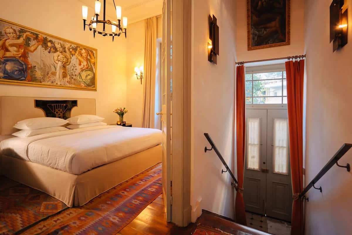 Une chambre d’hôtel avec un lit, un lustre, un tableau et un escalier.