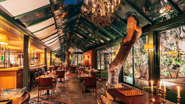 A restaurant with a high ceiling, glass walls, and a chandelier. Tables are set with candles and a chessboard.