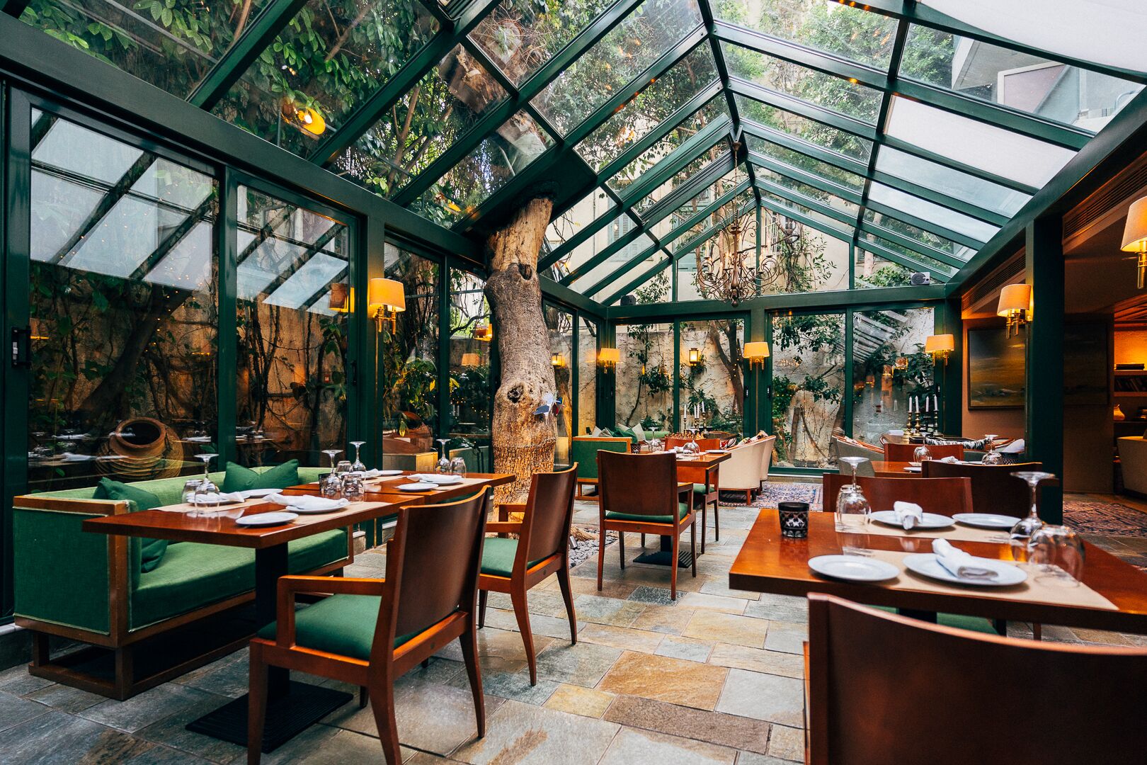 Un ristorante con soffitto in vetro, sedute verdi e pavimento in pietra.