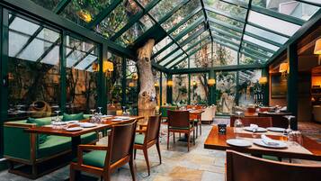 Een restaurant met een glazen dak, groene zitplaatsen en stenen vloeren.