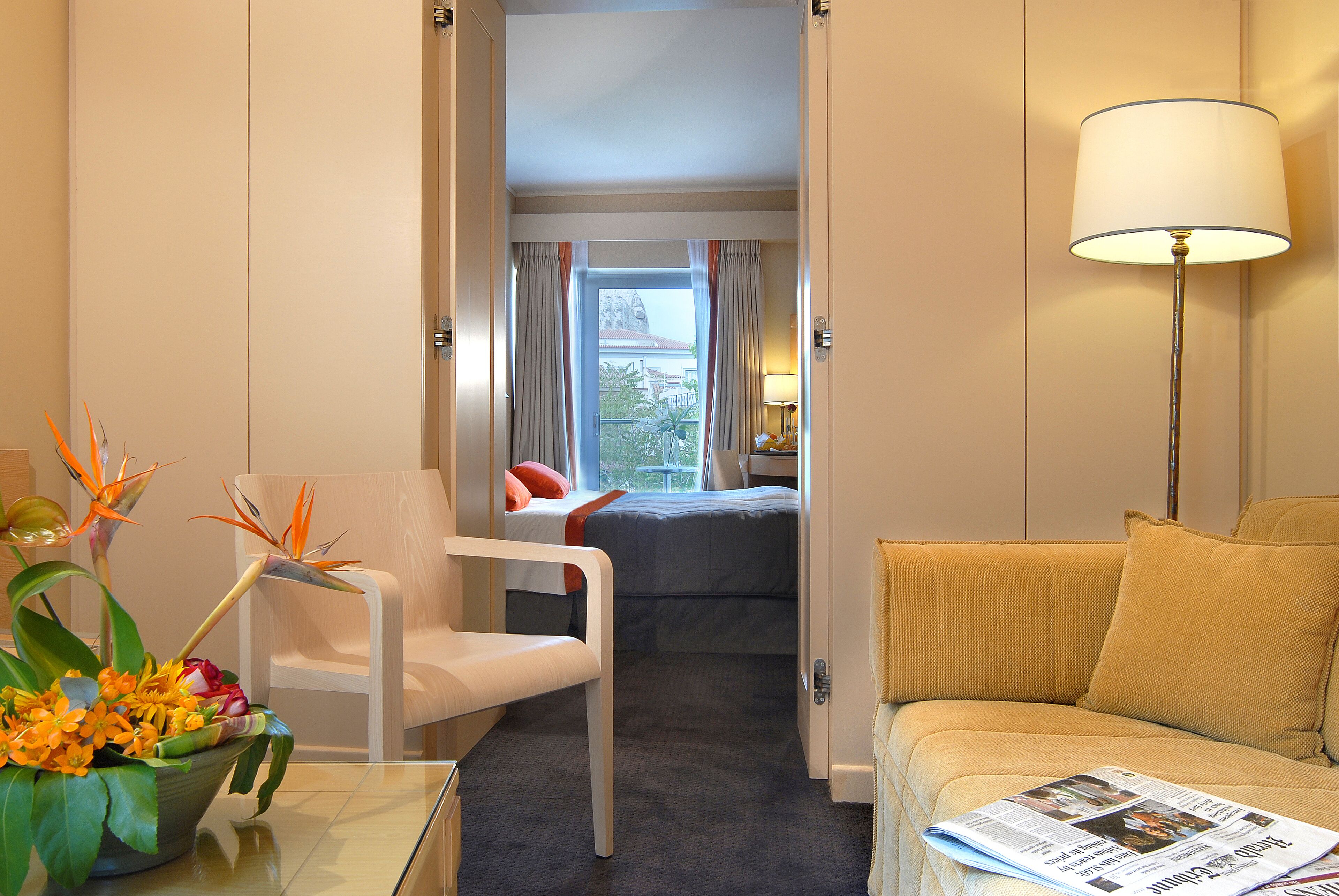 A hotel room with a bed, a chair, a sofa, a lamp, and a window with curtains.