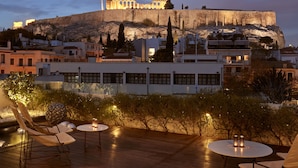 A rooftop terrace with a view of a historic building on a hill, furnished with chairs and tables.