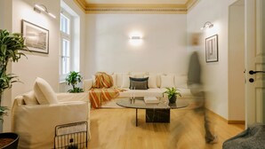 A living room with a sofa, armchair, coffee table, and potted plants.