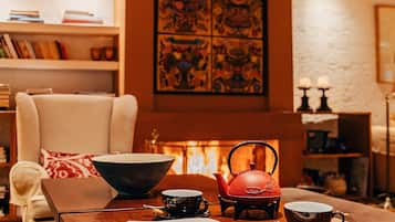 Una sala de estar acogedora con chimenea, una estantería y una mesa con tetera, tazas y un libro.