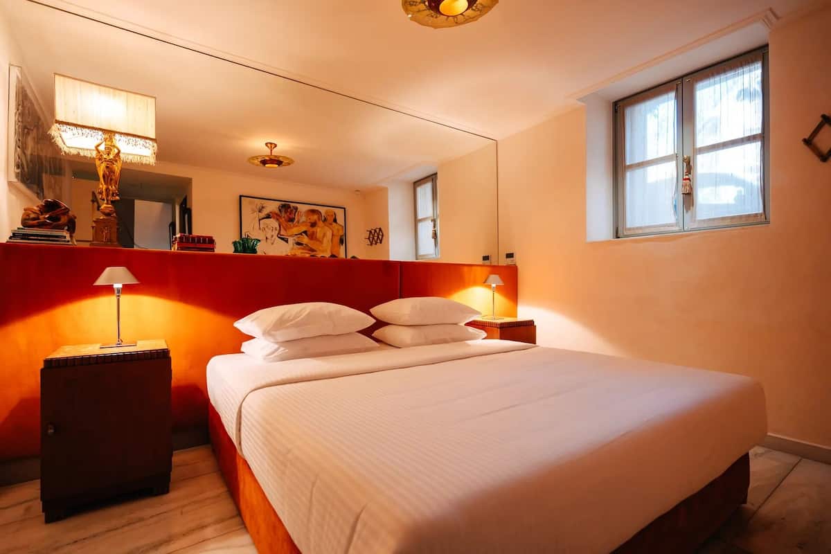 Une chambre d’hôtel avec un grand lit, une table de chevet, une lampe, un tableau au mur et une fenêtre avec des rideaux.