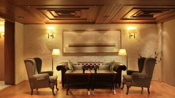 Une pièce chaleureuse avec un plafond en bois, un canapé en cuir, deux fauteuils, une table basse et des lampes fixées au mur.