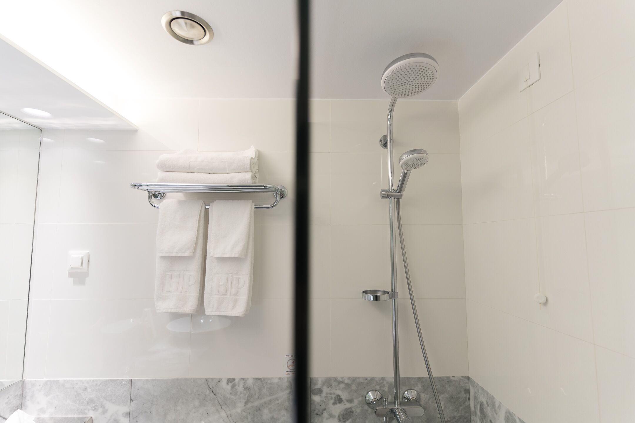 A modern bathroom with a glass shower enclosure, a marble-tiled floor, and a towel rack with folded towels.