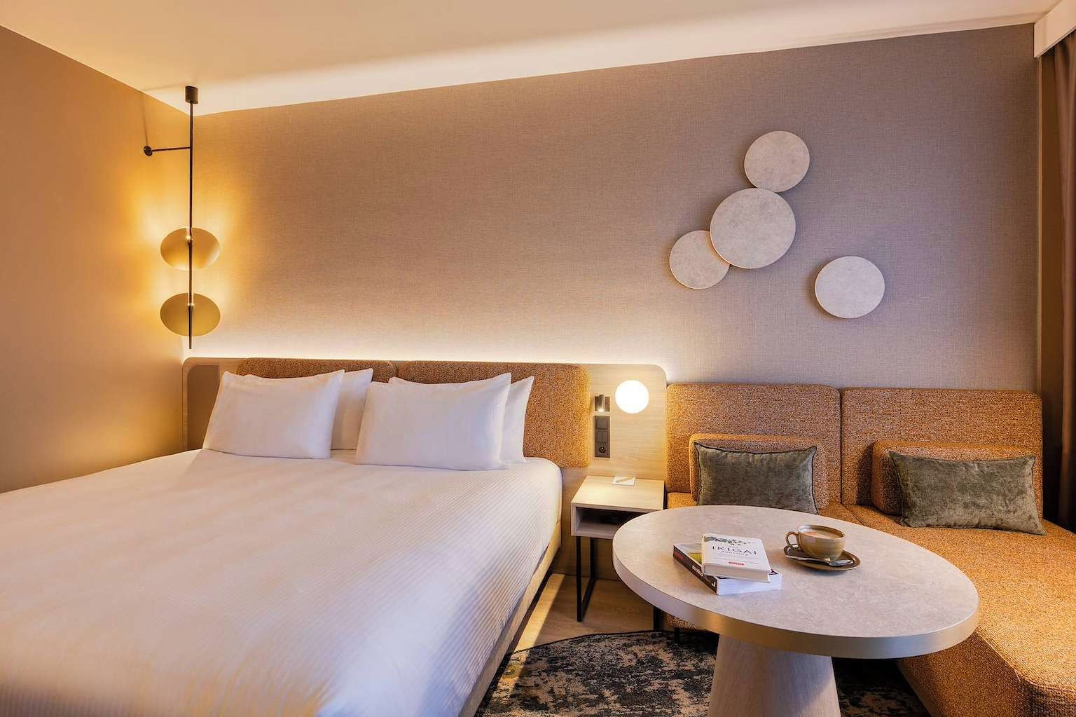 A hotel room with a large bed, a bedside table, a round coffee table, and a wall with circular decor.