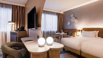 A hotel room with a bed, a desk, a chair, a TV, and a wall-mounted light fixture.