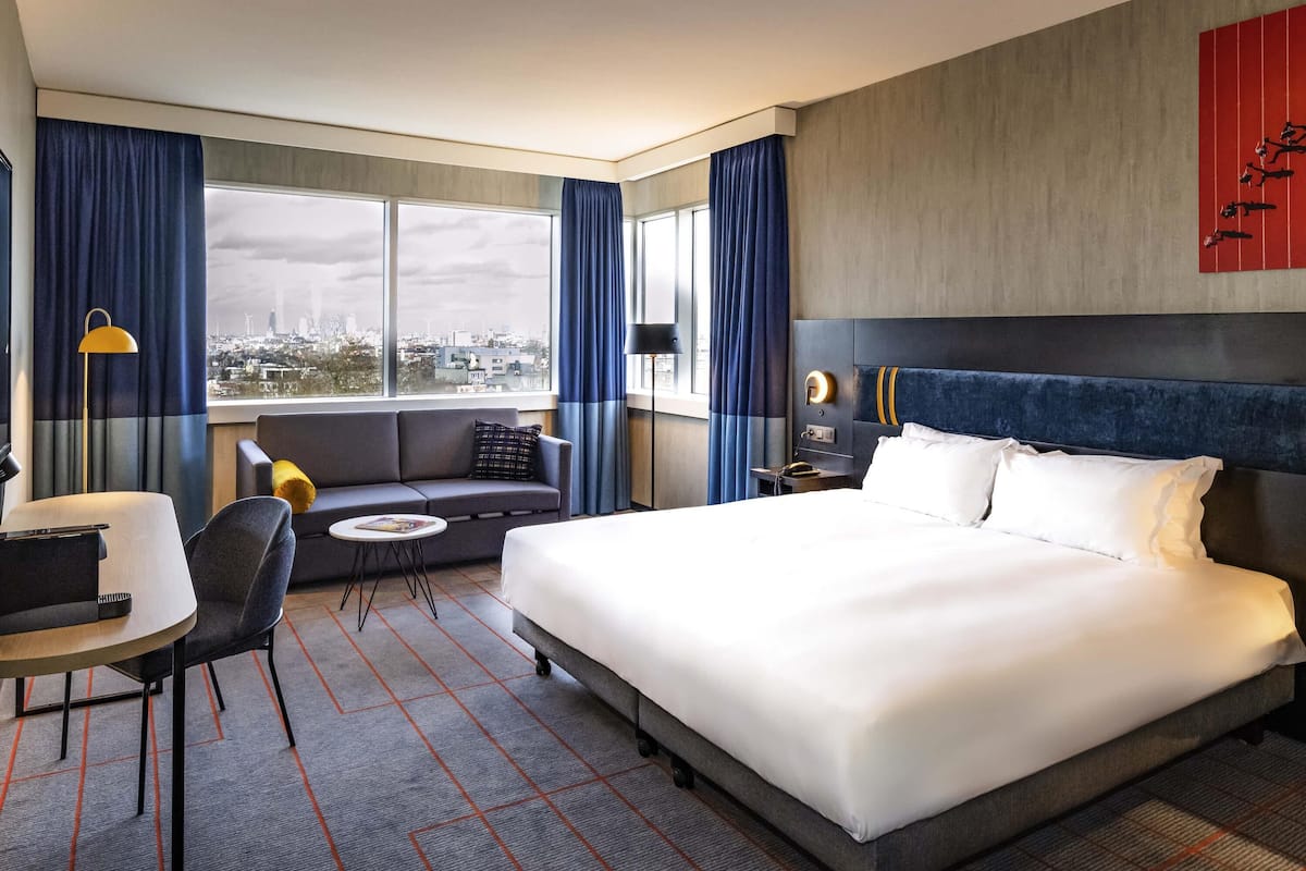 Habitación de hotel con una cama grande, un sofá, un escritorio y vistas a la ciudad.