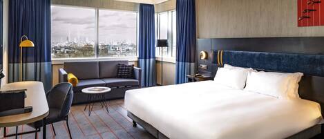 Habitación de hotel con una cama grande, un sofá, un escritorio y vistas a la ciudad.