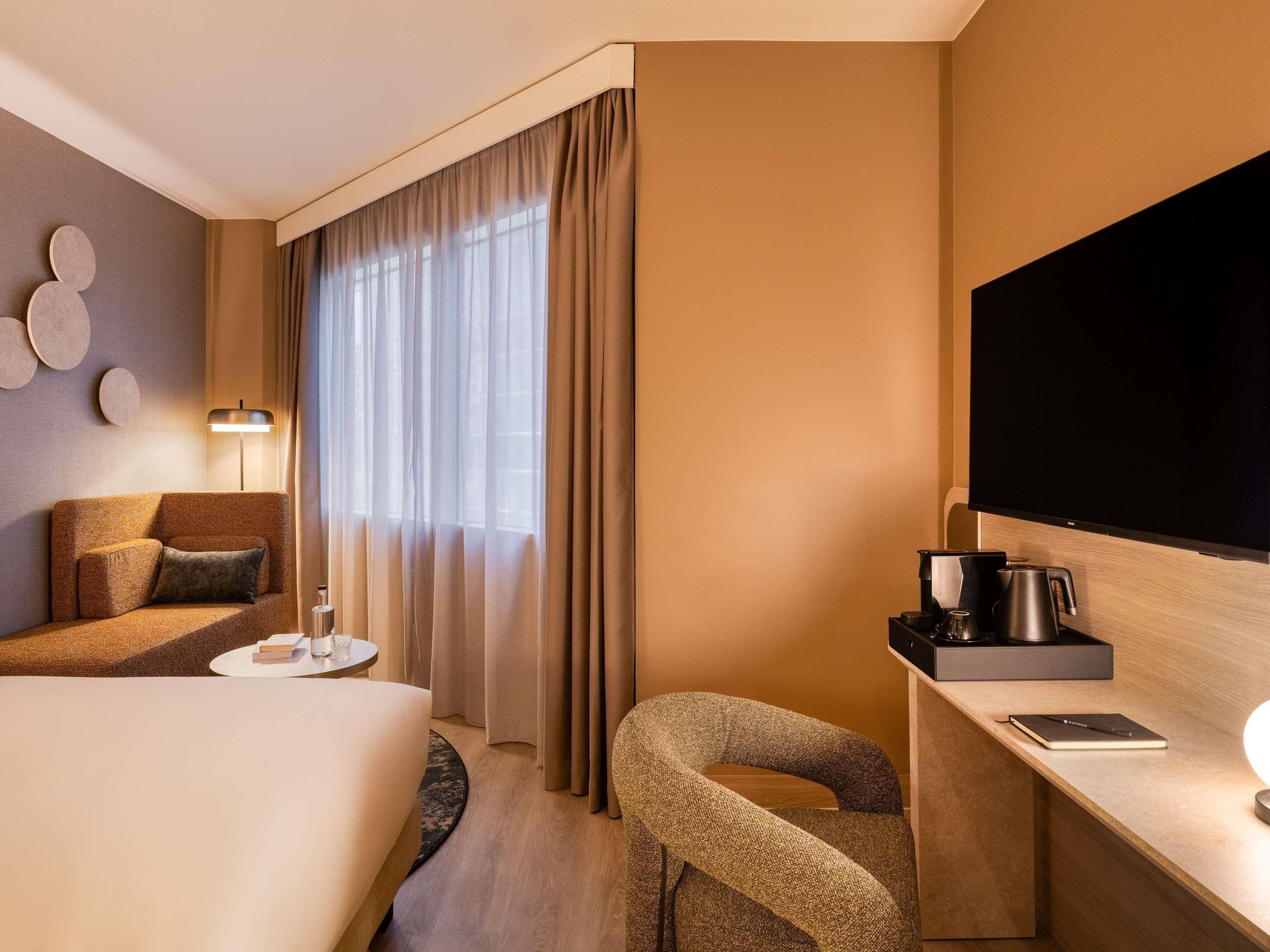 A hotel room with a bed, a desk with a flat-screen TV, a coffee maker, a chair, and a lamp.