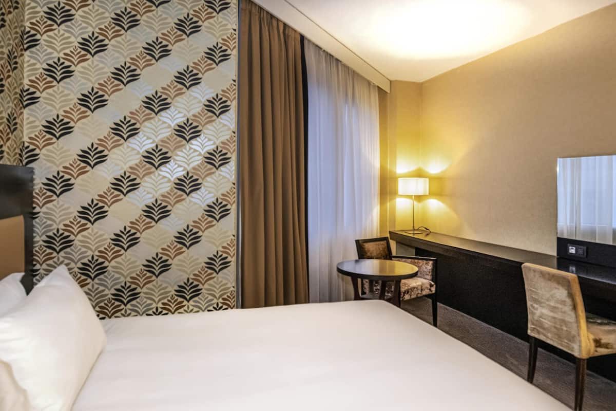 Una habitación de hotel con una cama grande, un escritorio con una silla, una lámpara y un televisor.
