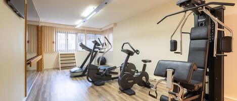 Un gimnasio con equipo de ejercicio, un televisor y ventanas amplias.
