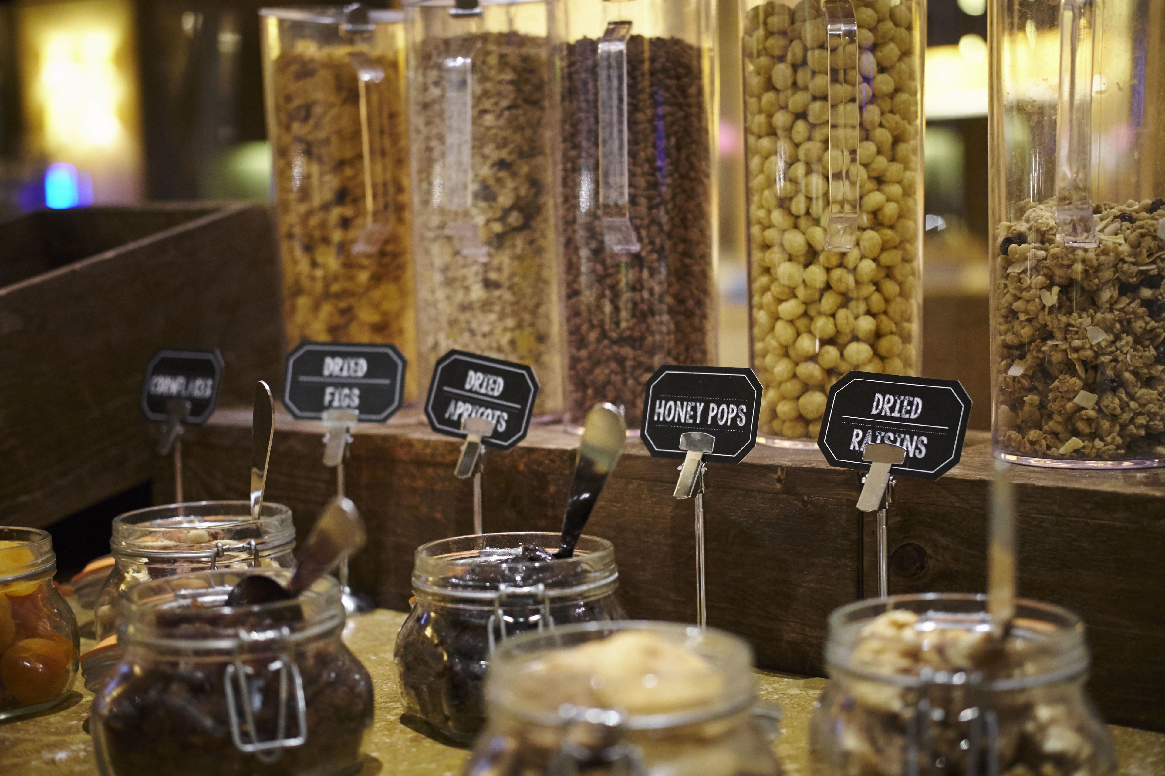A variety of dried fruits and nuts displayed in jars and containers with labels indicating their types.