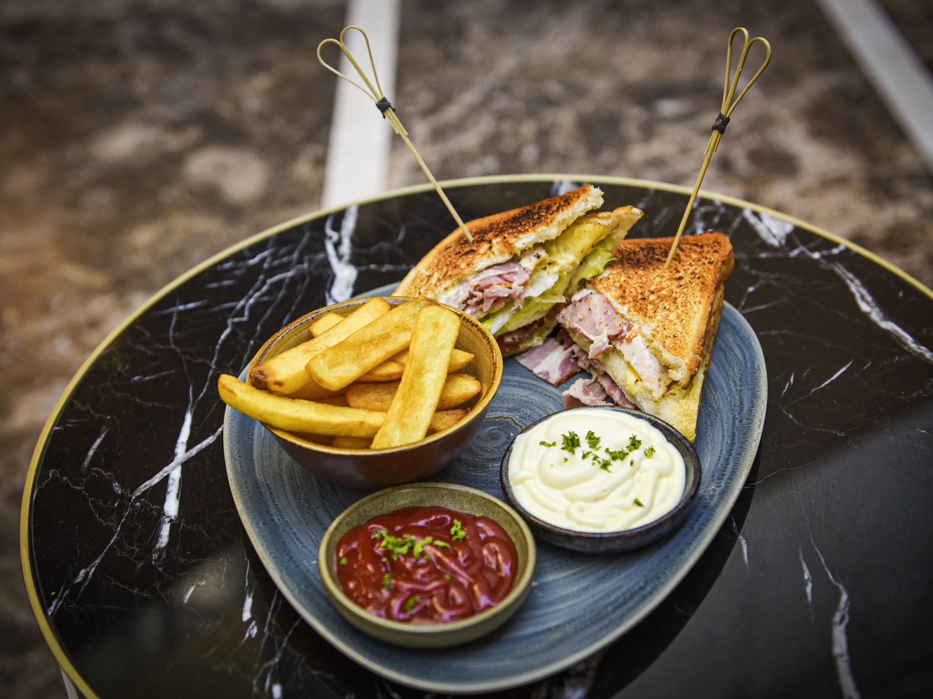 Een bord met een gegrilde sandwich, frietjes en twee dipsausjes.