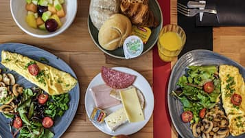 Una mesa de desayuno con diversos platos que incluyen huevos, queso, jamón y un bol de fruta.