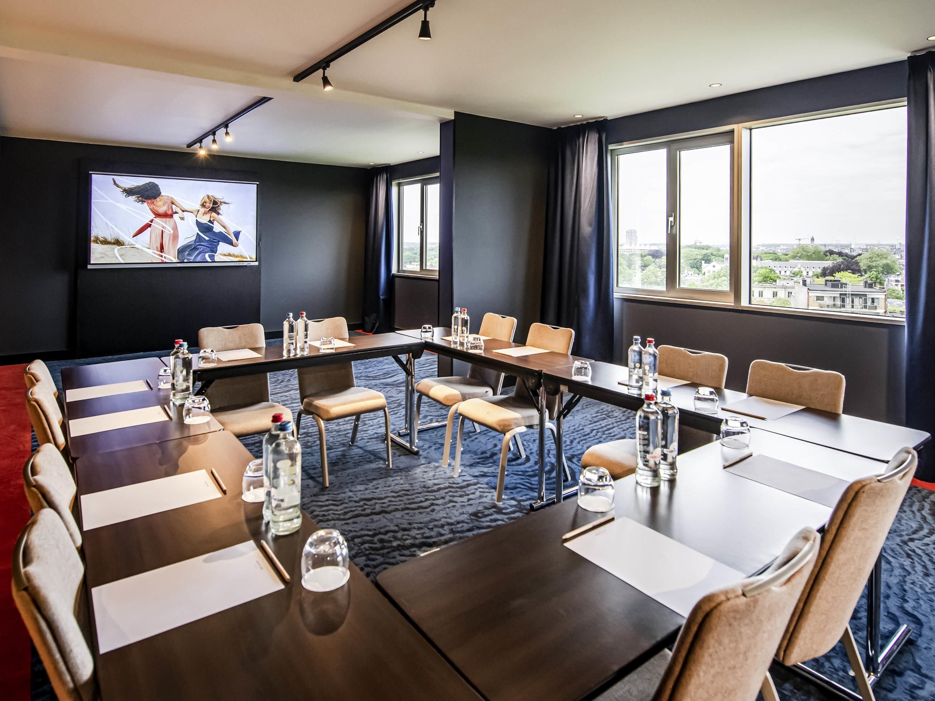 Une salle de conférence avec une longue table, des chaises, des bouteilles d’eau et une vue sur la ville.