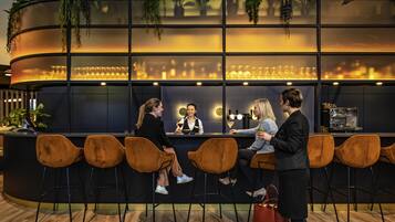 A bar area with a curved counter, multiple stools, and a barista preparing drinks.
