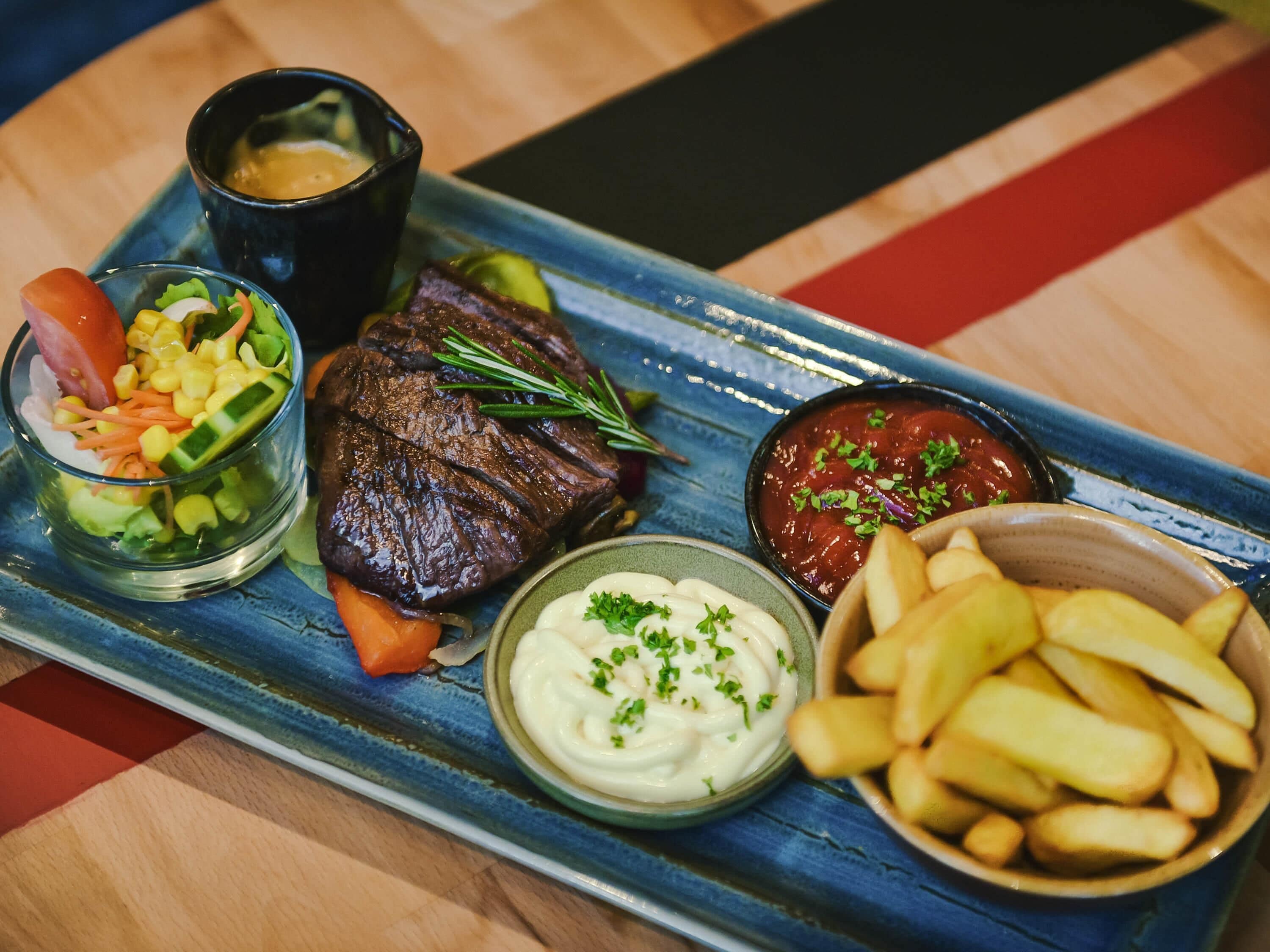 A meal with steak, vegetables, and sauces on a blue tray.