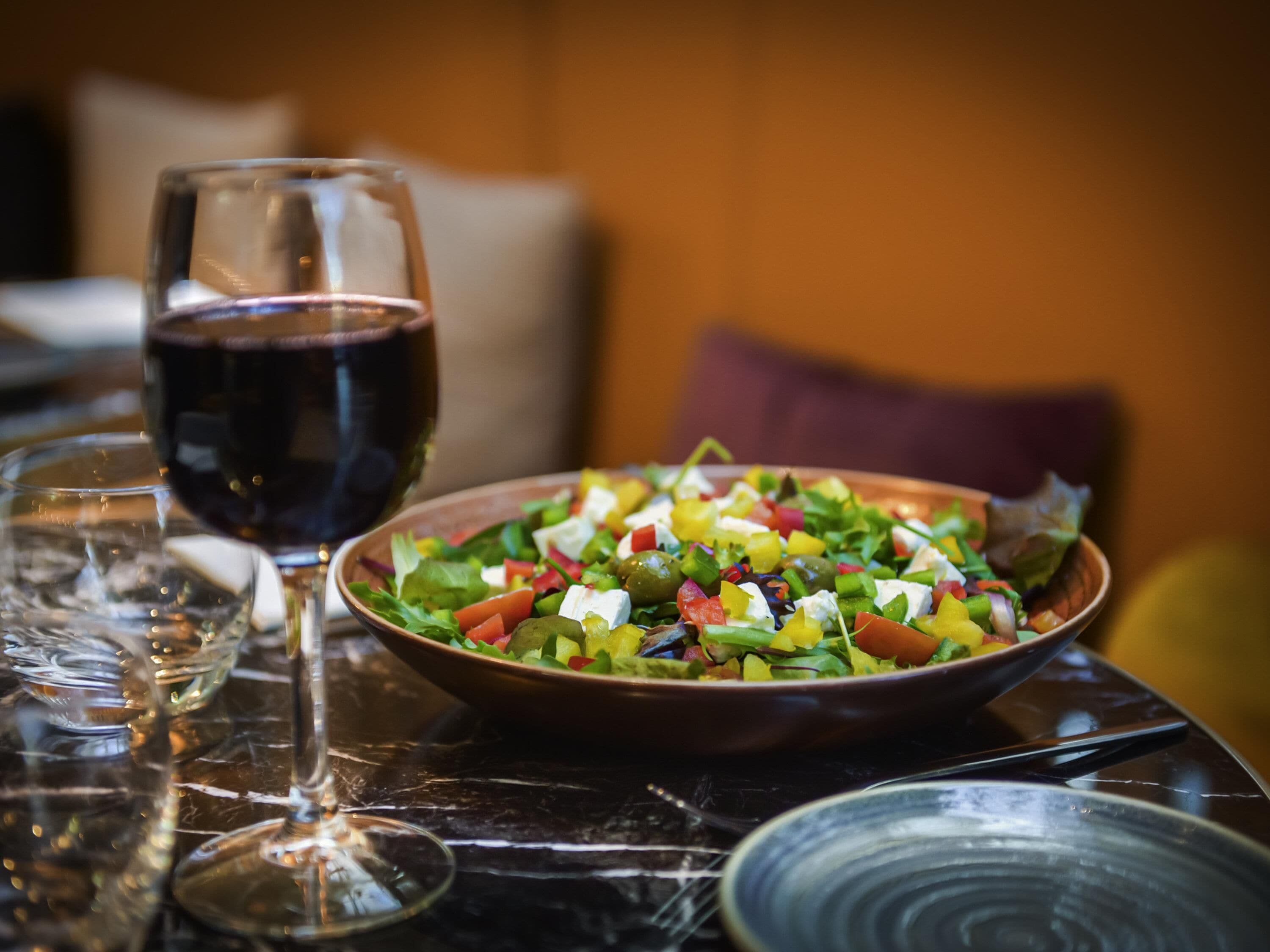 Une table avec un saladier rempli de salade, un verre de vin rouge et une assiette.
