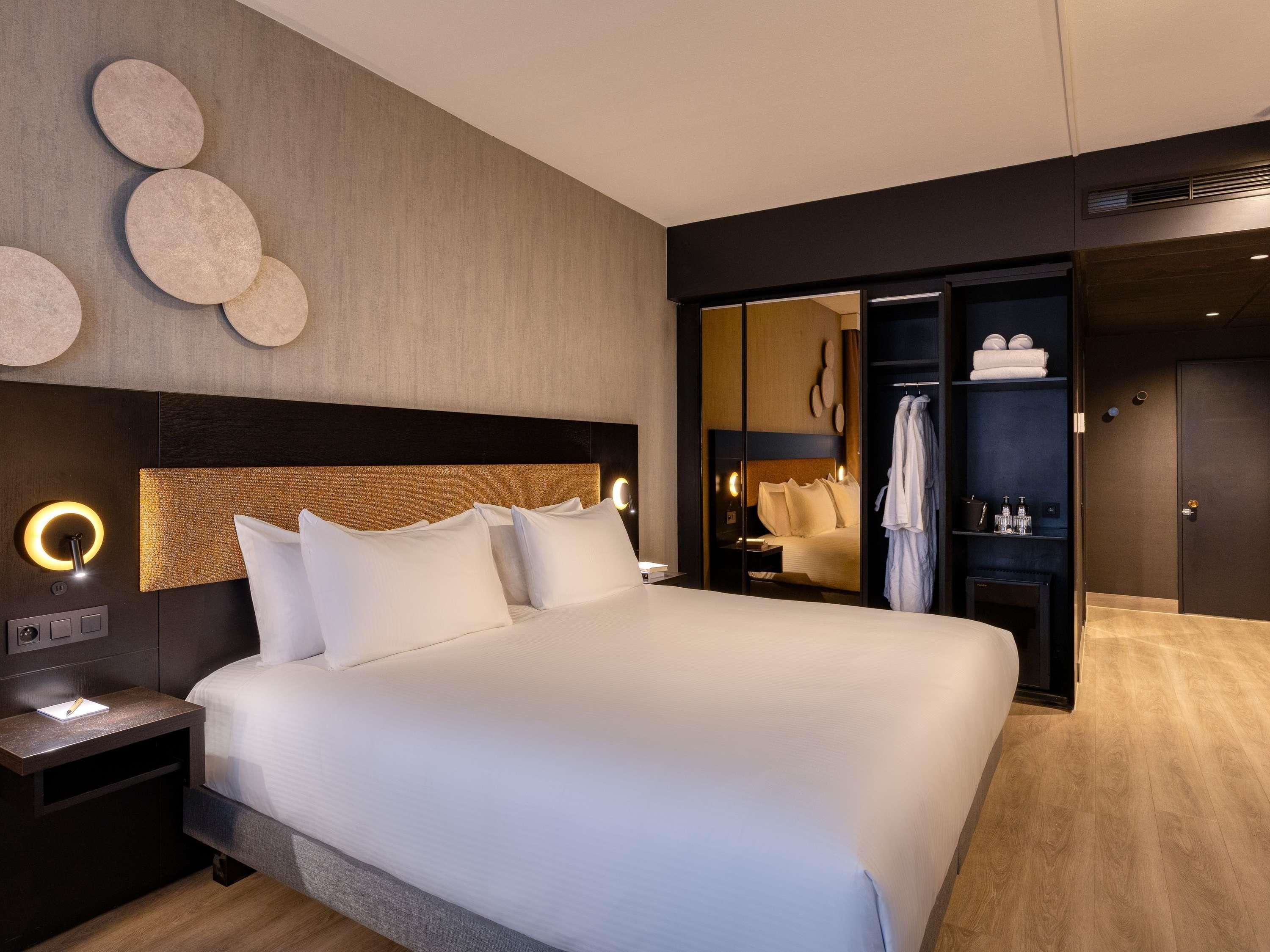 Ett modernt hotellrum med en stor säng, sängbord, en garderob och en spegel.