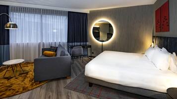 Una habitación de hotel moderna con una cama grande, un sofá, una mesita, una silla, un espejo redondo y un escritorio.