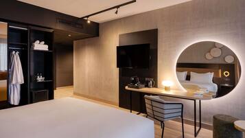 Une chambre d’hôtel moderne équipée d’un lit, d’un bureau, d’une chaise, d’une télévision et d’un miroir rond.