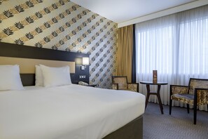 A hotel room with a large bed, a small table, two chairs, a nightstand, and a patterned wallpaper. - Pullman Antwerp (Antwerp)