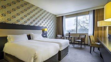 A hotel room with two beds, a desk, a chair, and a window with curtains.