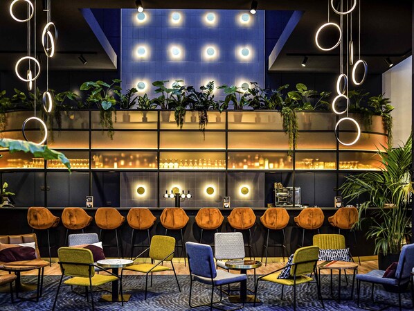 A modern lounge area with a variety of seating options, including sofas and chairs, and a bar area with a glass partition. - Pullman Antwerp (Antwerp)