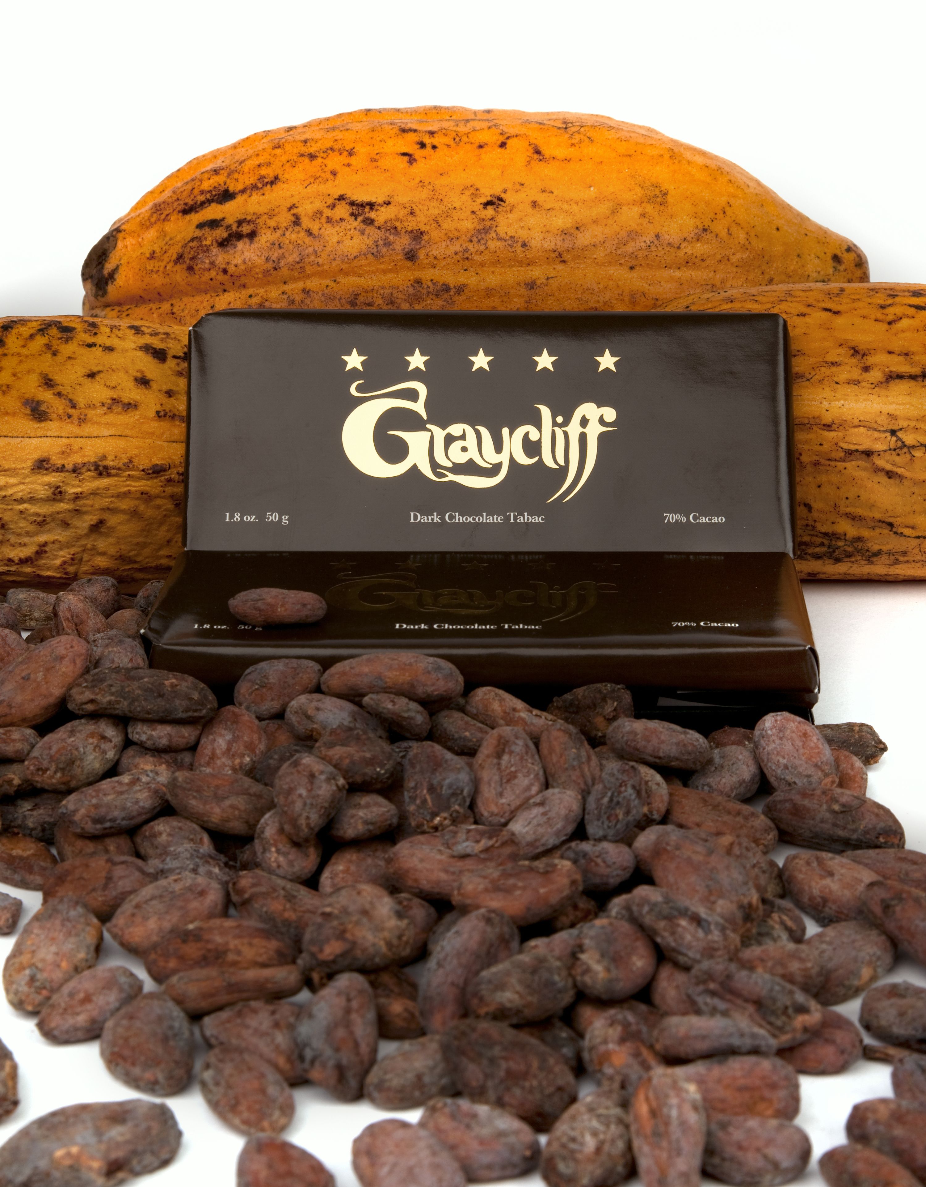 Une boîte de chocolats noirs Graycliff Tabac, avec en arrière-plan une banane et des fèves de cacao.