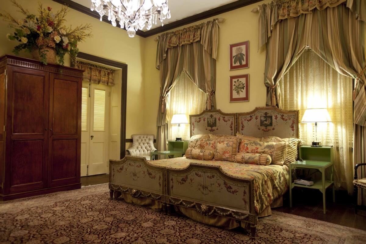 A traditional bedroom with a large bed, two bedside tables, a wooden wardrobe, and floral decorations.