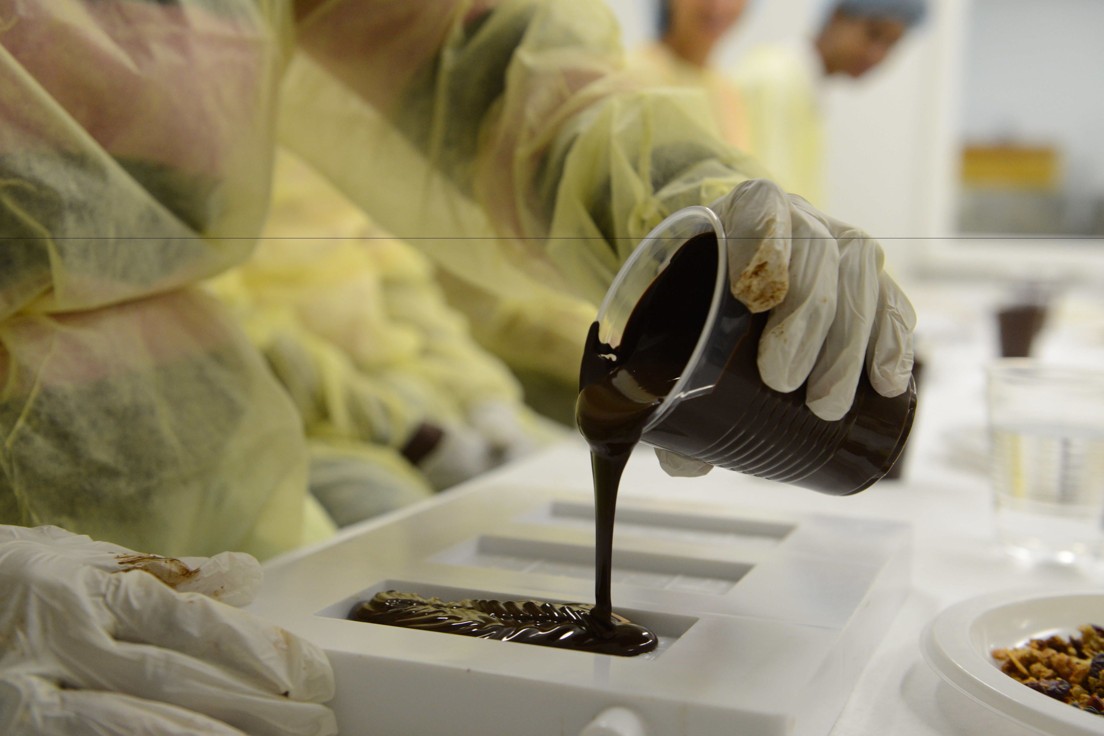 Une personne, vêtue d’une combinaison de protection, verse un liquide dans un moule.