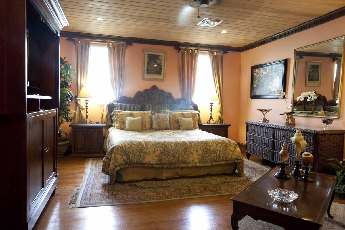 A spacious bedroom with a large bed, wooden floors, a dresser, and a mirror.
