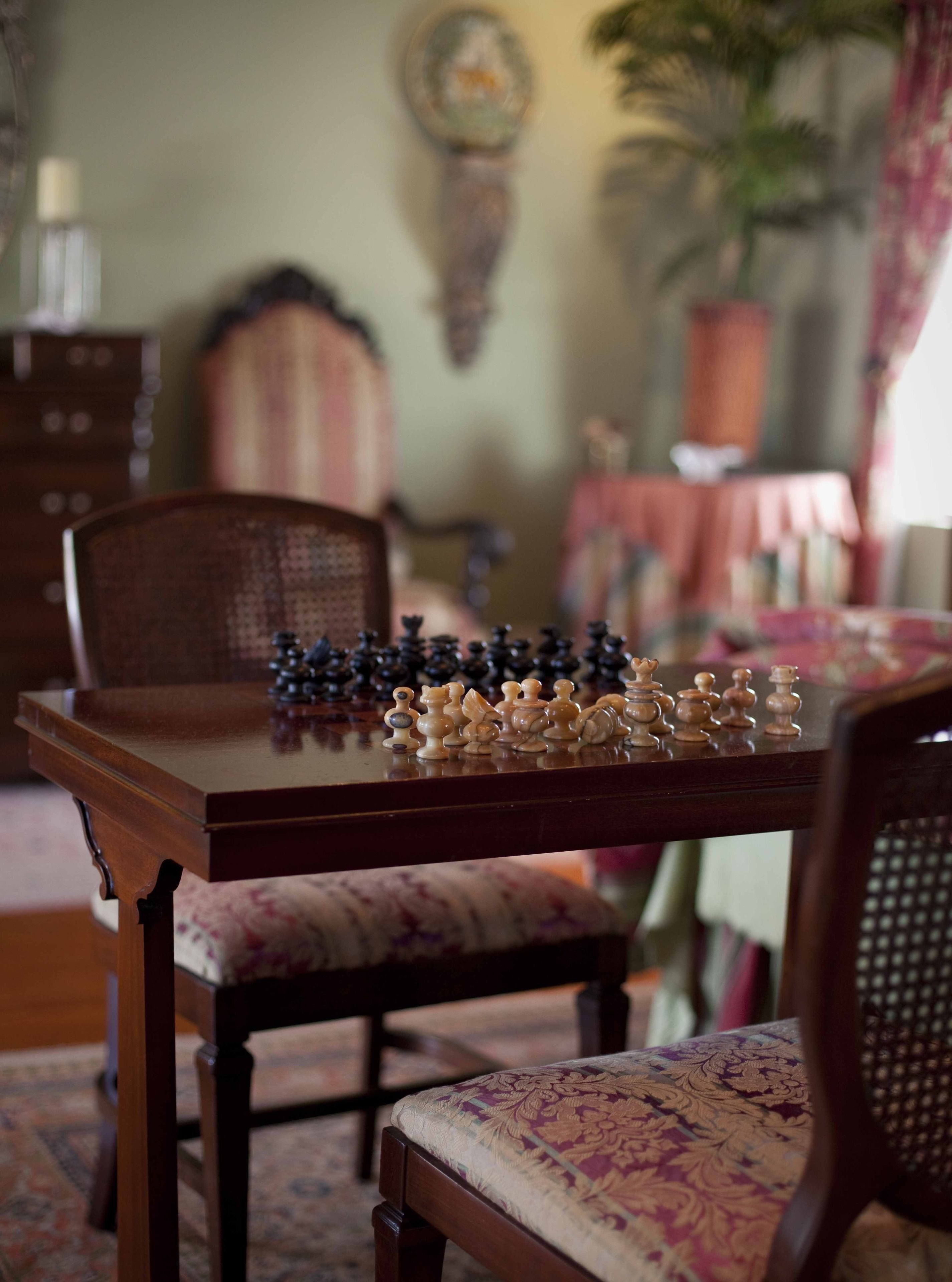 A chessboard on a wooden table with chairs around it.