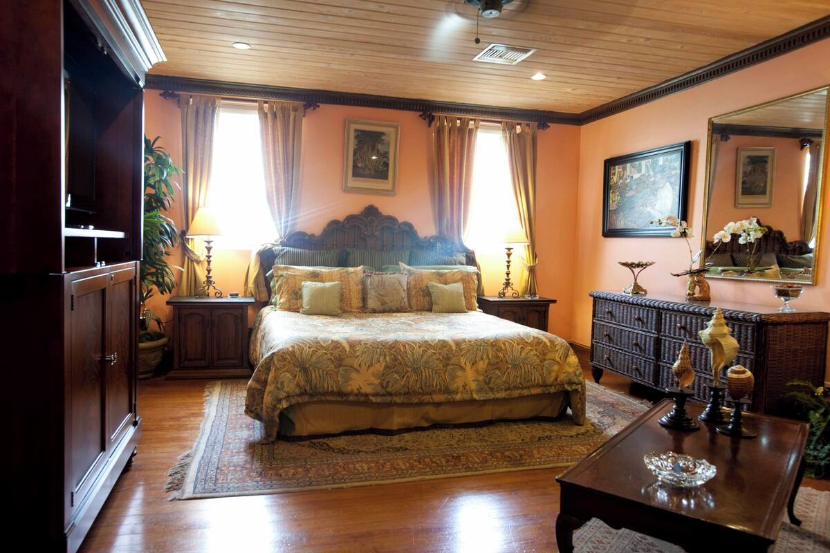 A bedroom with a large bed, a dresser, a nightstand, a mirror, and a decorative vase.