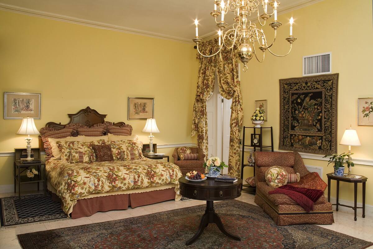A traditional bedroom with a large bed, a sofa, a chandelier, and a dining table.