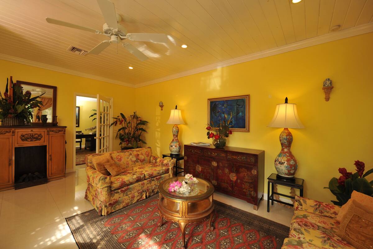 A living room with a yellow wall, a ceiling fan, a floral sofa, a coffee table, and a fireplace.