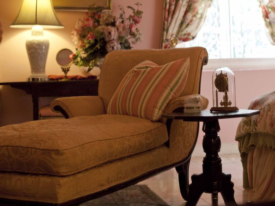 A cozy room with a floral-patterned sofa, a lamp, a small table with a decorative item, and a window with floral curtains.
