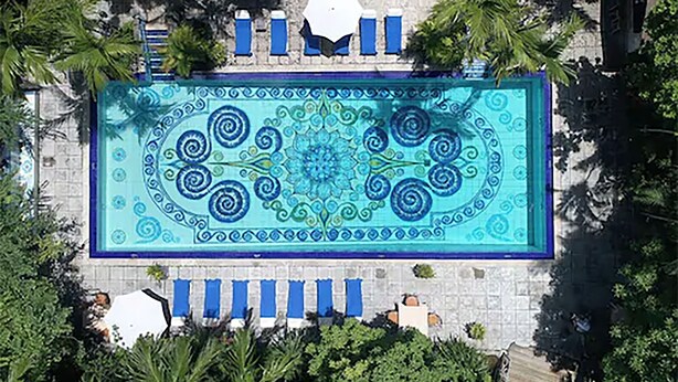 An aerial view of a rectangular swimming pool with a decorative tile pattern, surrounded by palm trees and blue lounge chairs. - Graycliff Hotel And Restaurant (Nassau)