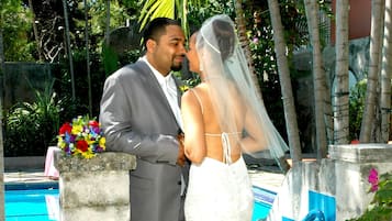 A couple standing by a pool with a stone pillar and a blue-tiled wall.